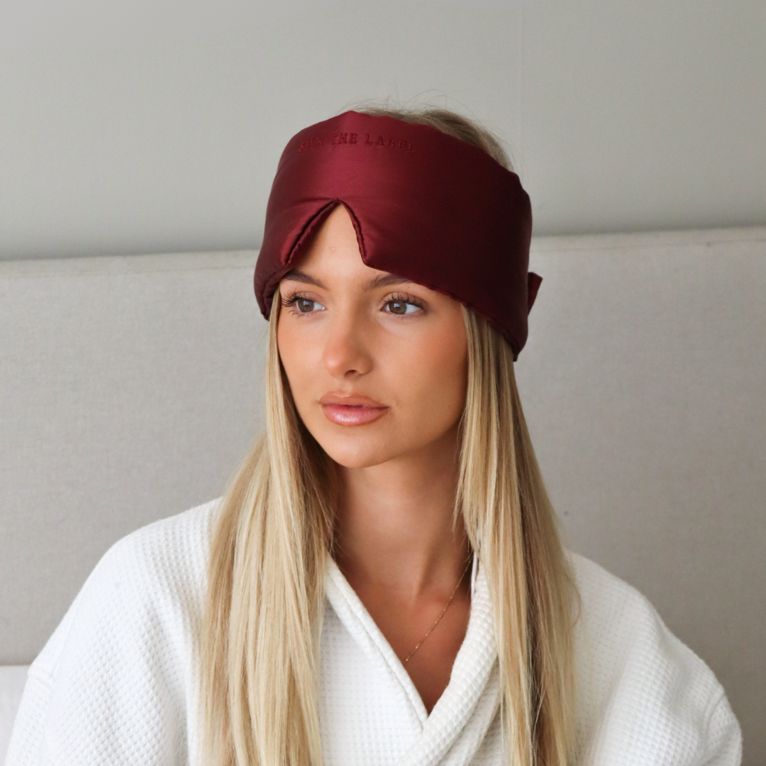 Woman wearing a red sleep mask and white robe in a neutral setting