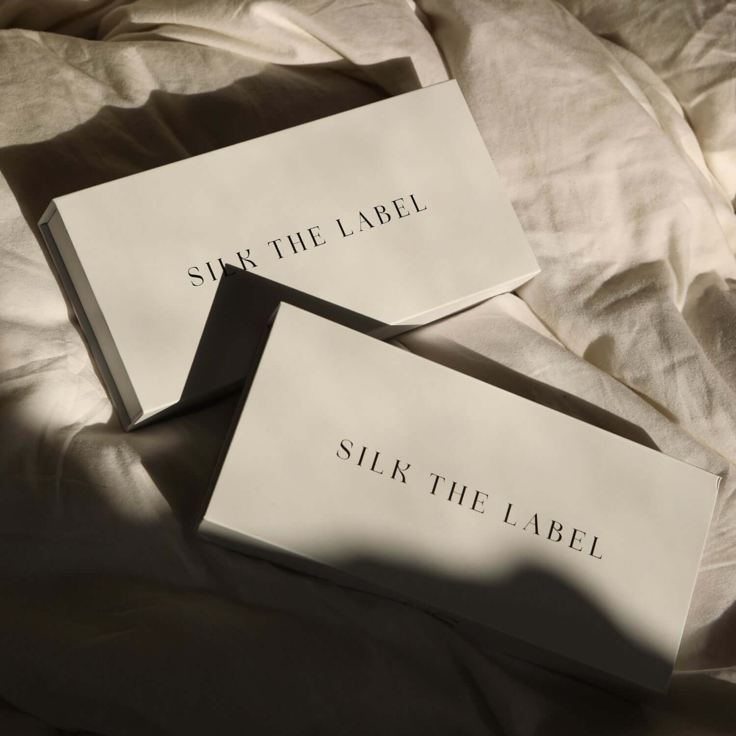 Silk The Label branded packaging boxes resting on soft cream bedding, showcasing luxury sleep accessory presentation.