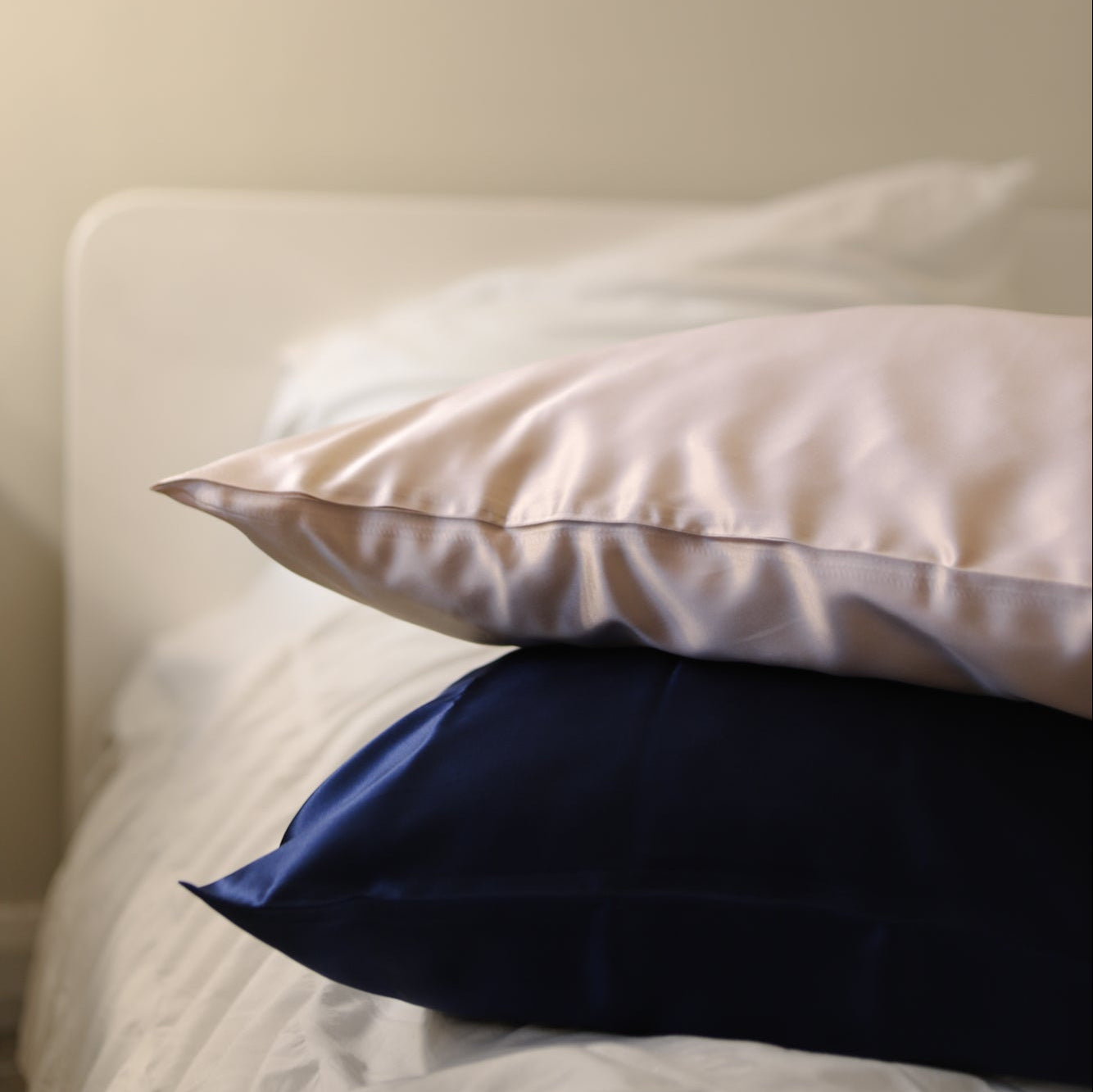 Two pillows, one white and one blue, stacked on a bed against a beige wall.